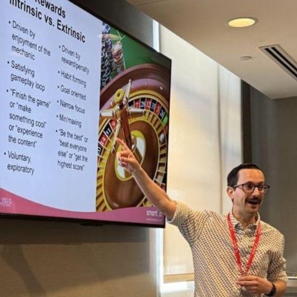 A man with glasses and a mustache pointing at a slideshow on a flatscreen tv.