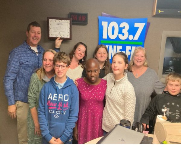 A group of kids and adults at a radio station smiling.